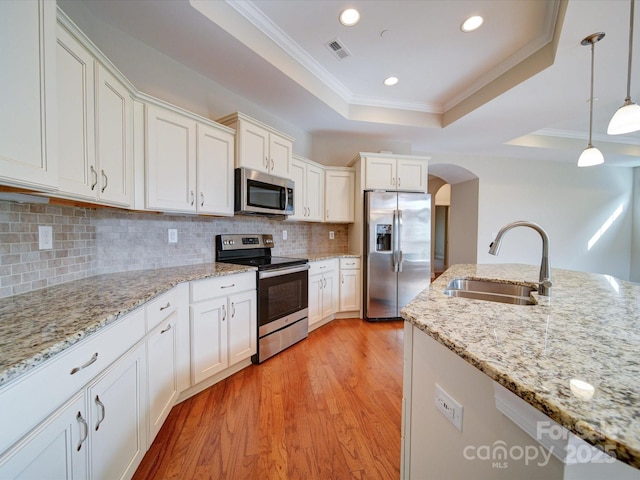 kitchen featuring pendant lighting, sink, appliances with stainless steel finishes, a tray ceiling, and light stone countertops