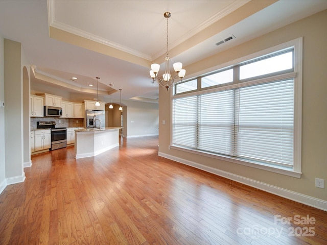 unfurnished living room with sink, light hardwood / wood-style flooring, a notable chandelier, a tray ceiling, and ornamental molding