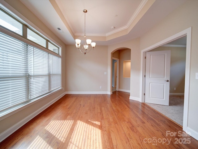 empty room featuring ornamental molding, a raised ceiling, light hardwood / wood-style flooring, and a notable chandelier