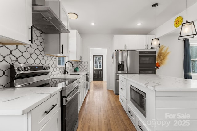 kitchen with white cabinetry, stainless steel appliances, a kitchen island, decorative light fixtures, and wall chimney exhaust hood