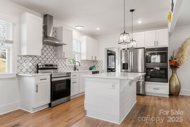 kitchen with pendant lighting, stainless steel appliances, a center island, white cabinets, and wall chimney exhaust hood