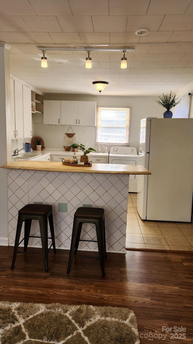 kitchen featuring freestanding refrigerator, white cabinetry, a peninsula, and a kitchen breakfast bar