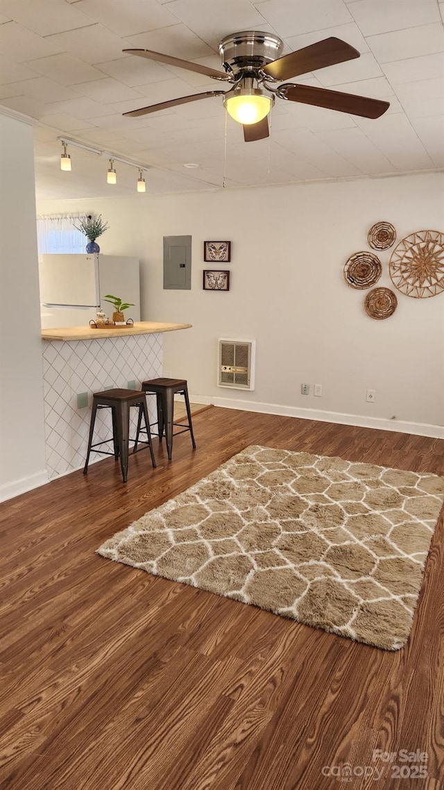 unfurnished dining area featuring electric panel, baseboards, a ceiling fan, wood finished floors, and heating unit