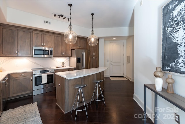 kitchen featuring a center island, hanging light fixtures, a kitchen breakfast bar, stainless steel appliances, and light stone countertops