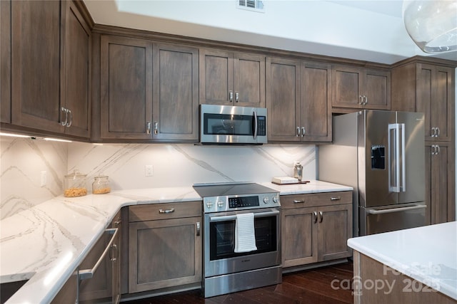 kitchen featuring tasteful backsplash, light stone countertops, appliances with stainless steel finishes, and dark brown cabinets