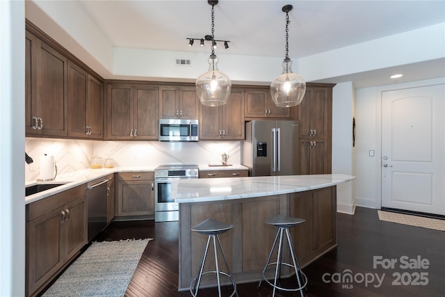 kitchen featuring appliances with stainless steel finishes, a kitchen bar, decorative backsplash, hanging light fixtures, and light stone countertops