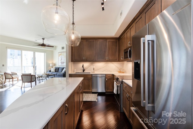 kitchen featuring sink, appliances with stainless steel finishes, hanging light fixtures, light stone countertops, and decorative backsplash