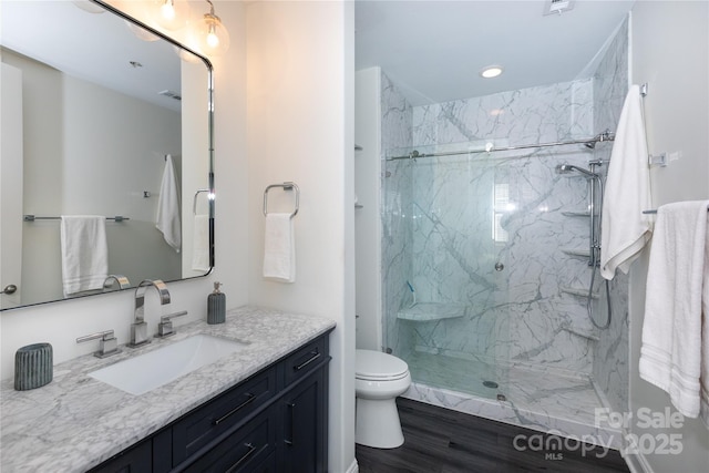 bathroom featuring vanity, tiled shower, hardwood / wood-style floors, and toilet