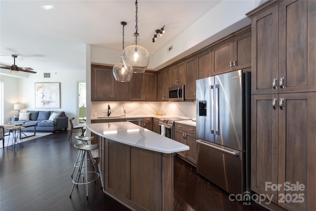 kitchen featuring stainless steel appliances, a kitchen island, open floor plan, light countertops, and pendant lighting