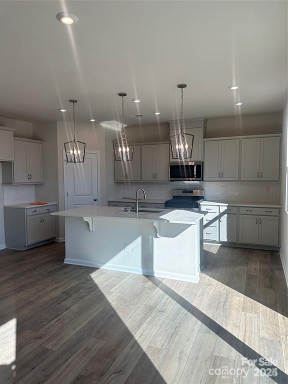 kitchen with dark wood-type flooring, stainless steel appliances, a chandelier, and a center island with sink