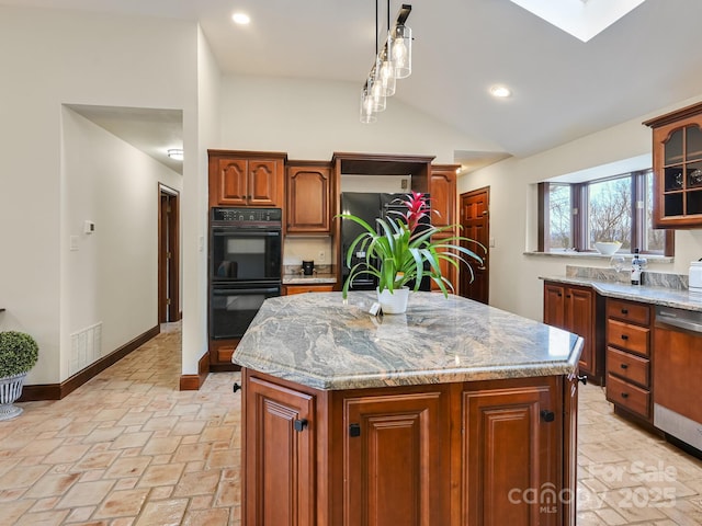 kitchen with a kitchen island, vaulted ceiling with skylight, decorative light fixtures, black appliances, and light stone countertops