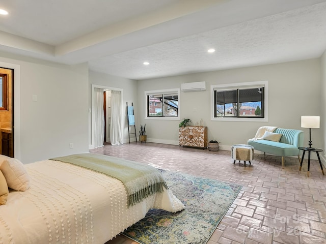 bedroom featuring ensuite bathroom, a wall unit AC, and a textured ceiling