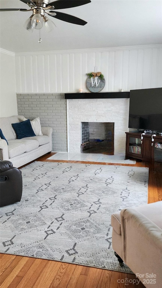 living room featuring ceiling fan, ornamental molding, a fireplace, and light hardwood / wood-style flooring