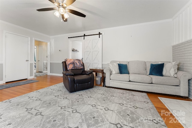 living room featuring ceiling fan, wood-type flooring, a barn door, and ornamental molding