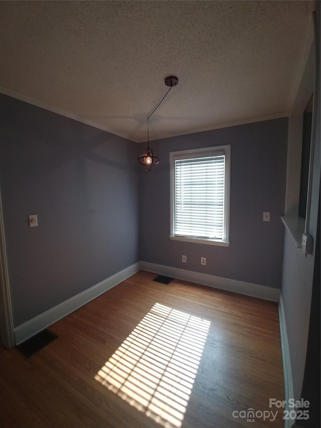 unfurnished dining area featuring hardwood / wood-style flooring, ornamental molding, and a textured ceiling