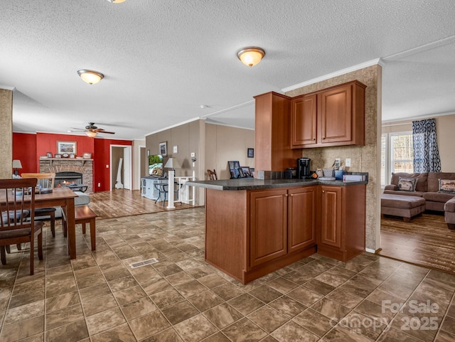 kitchen featuring ceiling fan, a fireplace, kitchen peninsula, and a textured ceiling