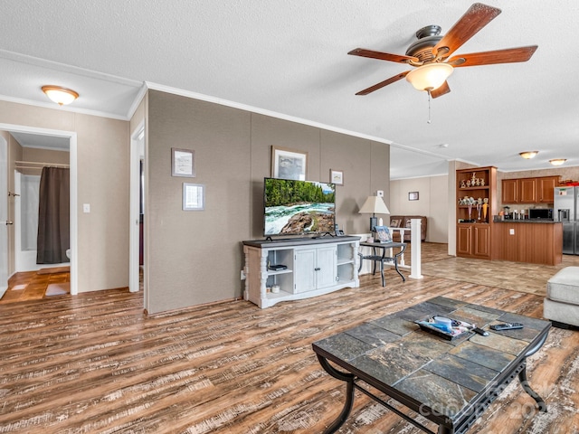 living room featuring ceiling fan, wood-type flooring, ornamental molding, and a textured ceiling