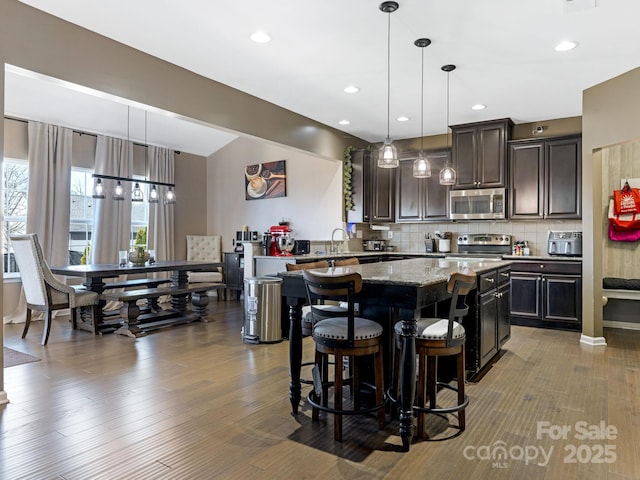 kitchen with dark brown cabinetry, a kitchen breakfast bar, appliances with stainless steel finishes, decorative backsplash, and a center island