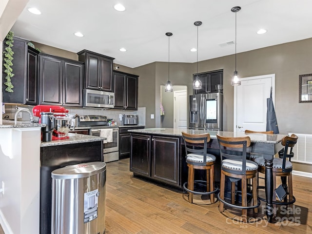 kitchen with stainless steel appliances, a kitchen breakfast bar, light wood-style floors, backsplash, and a center island