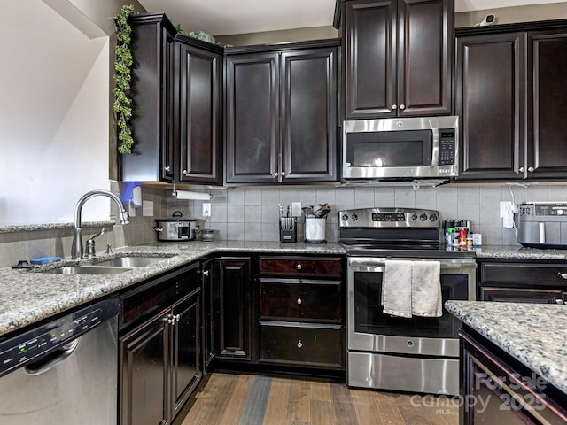 kitchen featuring stainless steel appliances, light stone counters, a sink, and decorative backsplash