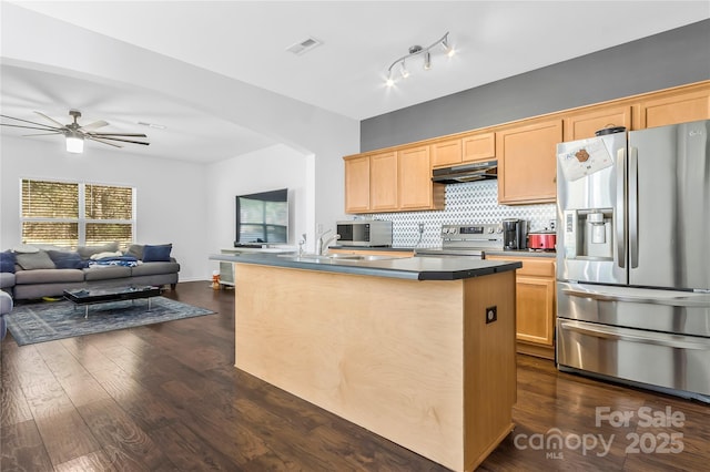 kitchen with appliances with stainless steel finishes, dark hardwood / wood-style floors, tasteful backsplash, an island with sink, and light brown cabinetry