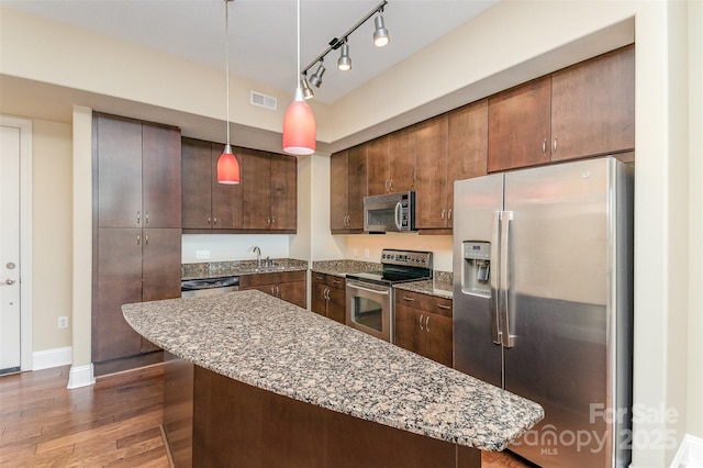 kitchen with pendant lighting, dark wood-type flooring, appliances with stainless steel finishes, light stone counters, and dark brown cabinetry