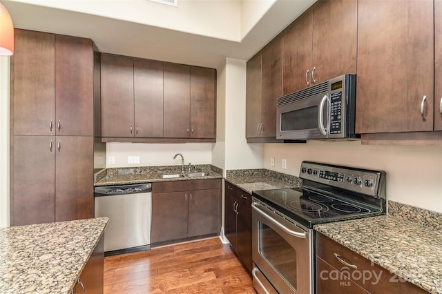 kitchen with dark brown cabinetry, sink, dark stone counters, dark hardwood / wood-style flooring, and stainless steel appliances