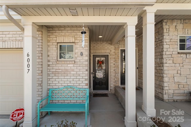 entrance to property featuring a garage, brick siding, and covered porch