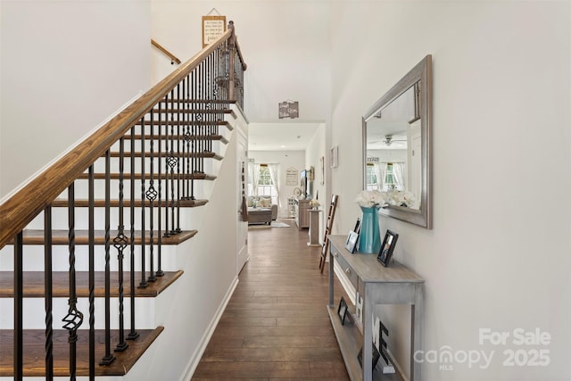 staircase featuring a towering ceiling, baseboards, and wood-type flooring