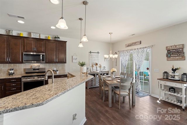 kitchen with tasteful backsplash, dark wood finished floors, stainless steel appliances, a barn door, and dark brown cabinets