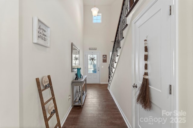 hall featuring dark wood finished floors, baseboards, stairs, and a towering ceiling