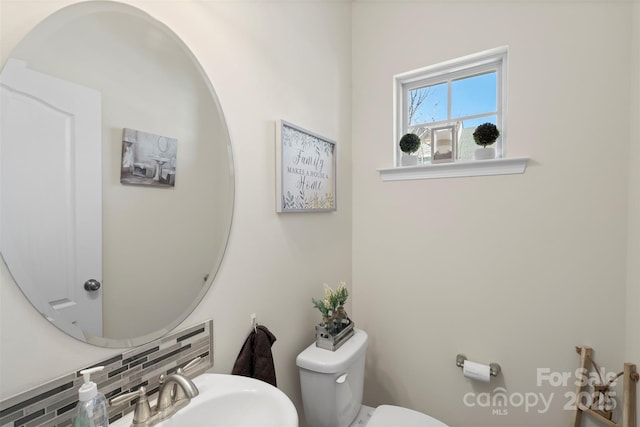 half bath with backsplash, toilet, and a sink