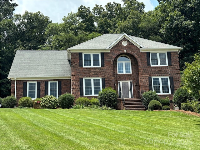 colonial inspired home featuring brick siding, a front yard, and a shingled roof