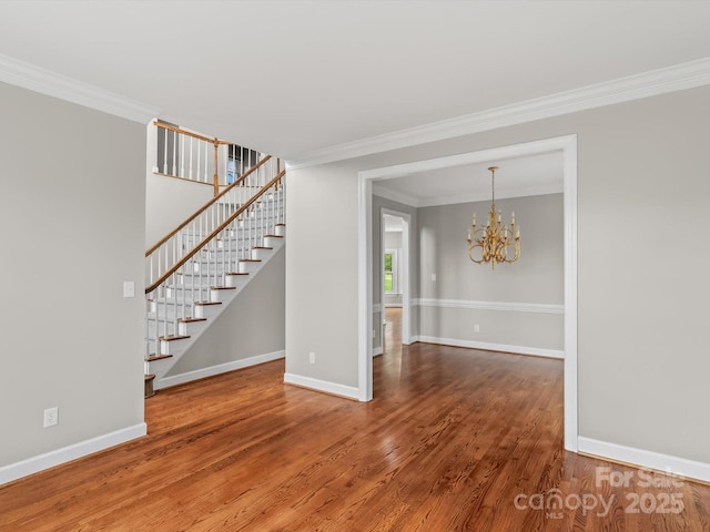 spare room with a notable chandelier, wood finished floors, baseboards, stairway, and crown molding