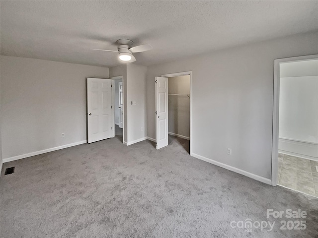 unfurnished bedroom with a spacious closet, a textured ceiling, carpet flooring, a closet, and ceiling fan