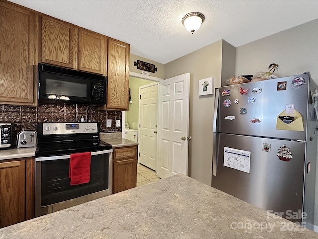 kitchen featuring light tile patterned flooring, tasteful backsplash, washer / dryer, stainless steel appliances, and a textured ceiling