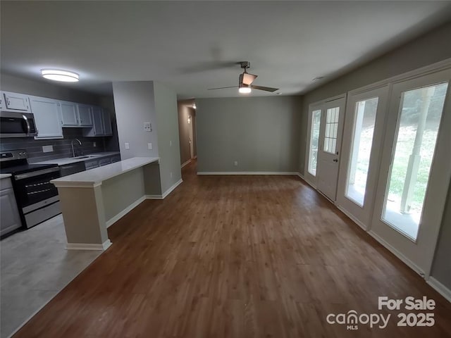 kitchen with tasteful backsplash, wood-type flooring, white cabinetry, kitchen peninsula, and stainless steel appliances