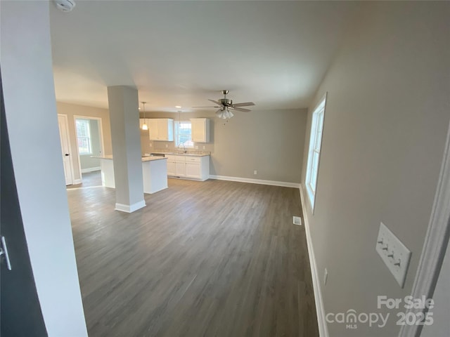 unfurnished living room with ceiling fan, wood finished floors, a sink, visible vents, and baseboards