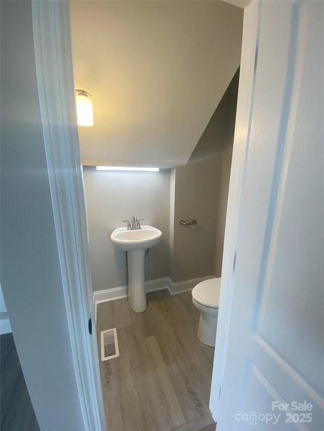 bathroom with lofted ceiling, toilet, wood finished floors, visible vents, and baseboards