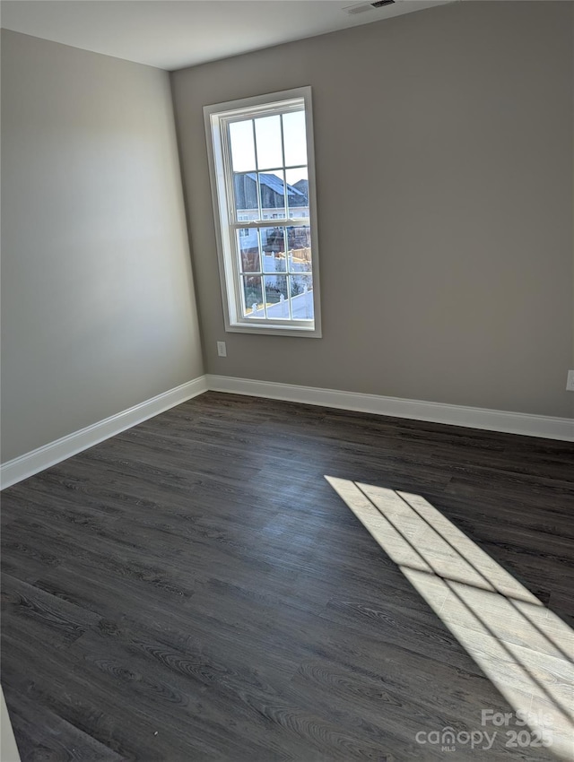 spare room with dark wood-style flooring, visible vents, and baseboards