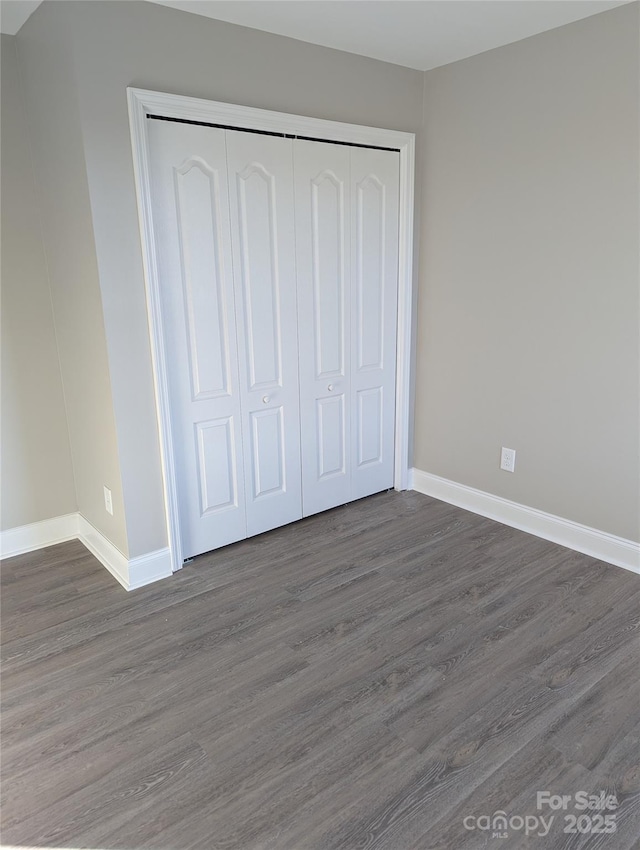 unfurnished bedroom with baseboards, dark wood finished floors, and a closet