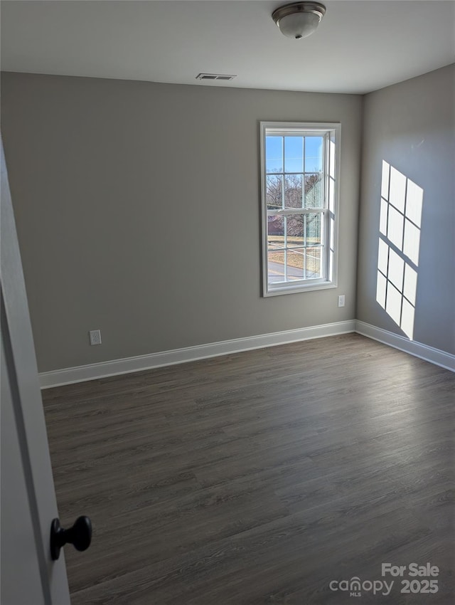 spare room with dark wood-style floors, visible vents, and baseboards