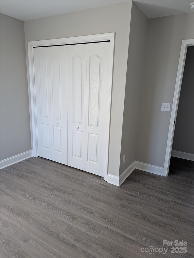 unfurnished bedroom featuring dark wood-type flooring, a closet, and baseboards