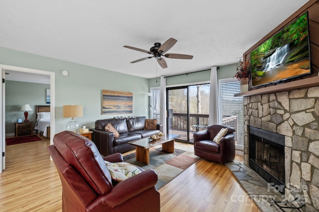 living area with a stone fireplace, light wood-style flooring, and a ceiling fan