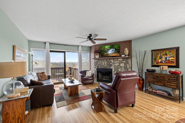 living area with light wood finished floors, a ceiling fan, a textured ceiling, and a stone fireplace