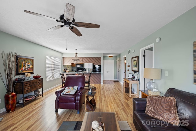 living room with a textured ceiling, ceiling fan, baseboards, and light wood-style floors