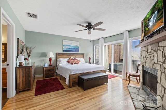 bedroom with a textured ceiling, a stone fireplace, visible vents, light wood-style floors, and access to outside