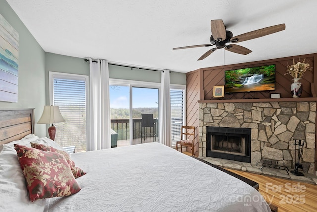 bedroom featuring access to outside, a textured ceiling, wood finished floors, and a stone fireplace