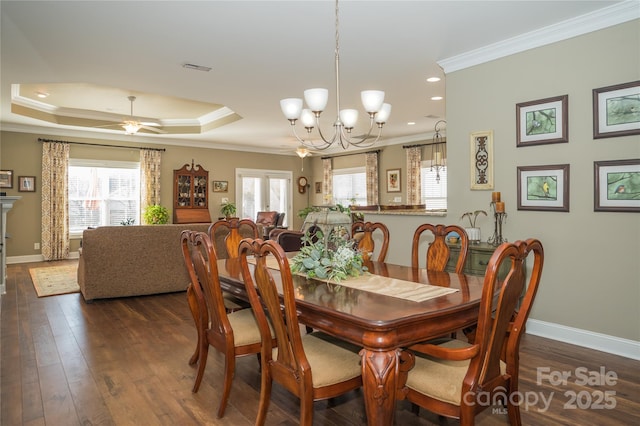 dining area with a wealth of natural light, dark wood-type flooring, ornamental molding, and a raised ceiling