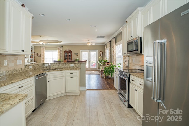 kitchen with appliances with stainless steel finishes, white cabinetry, backsplash, light stone counters, and kitchen peninsula